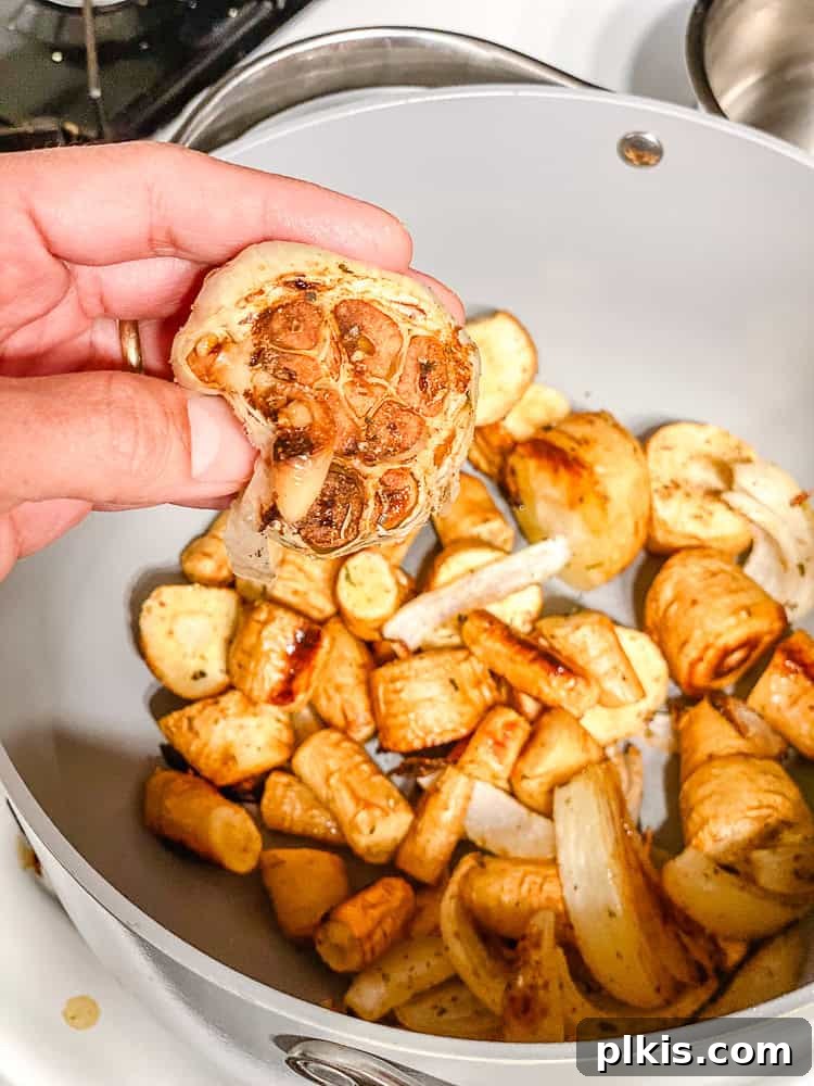Maple-Kissed Roasted Parsnip Soup 5 Roasted garlic being squeezed into a pot with other roasted vegetables.