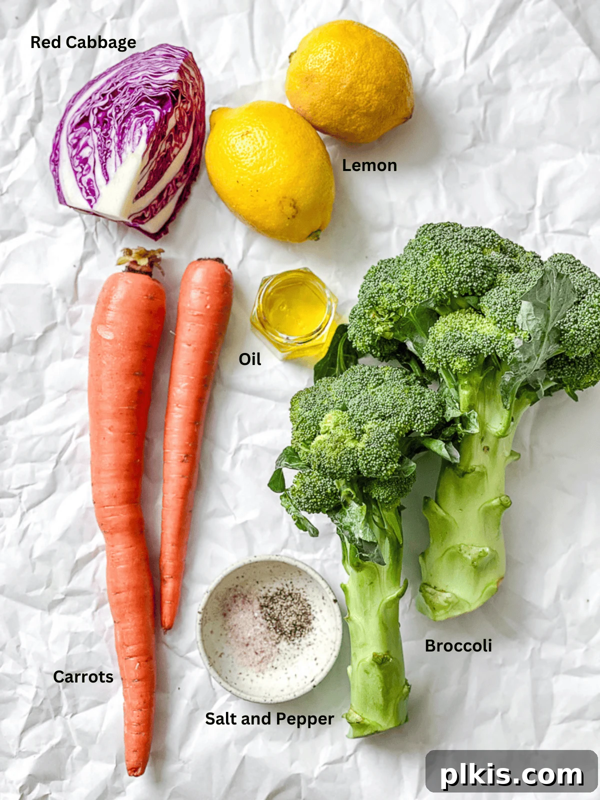 Zesty Broccoli Slaw 3 All the fresh ingredients for broccoli slaw, including broccoli, carrots, red cabbage, lemons, and olive oil, neatly laid out on a clean white surface.