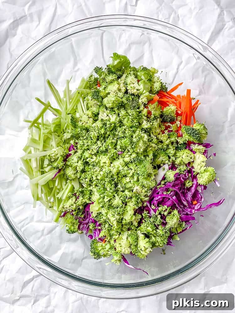Zesty Broccoli Slaw 5 A process shot showing a large bowl with various chopped vegetables, including broccoli, carrots, and cabbage, ready for dressing.