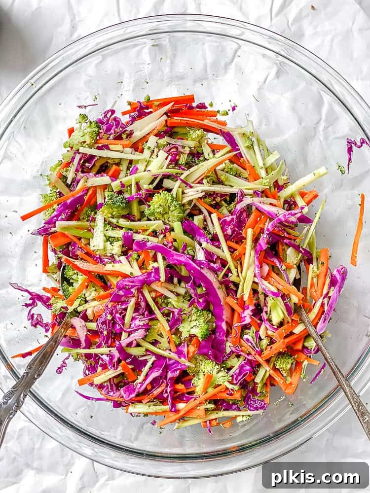 Zesty Broccoli Slaw 7 A process shot showing a hand actively mixing the broccoli slaw ingredients and dressing together in a large bowl.