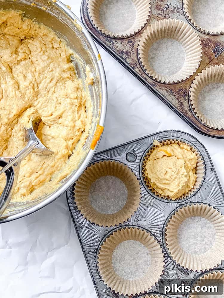 Butternut squash cupcake batter being carefully scooped into a muffin tin lined with paper cups.