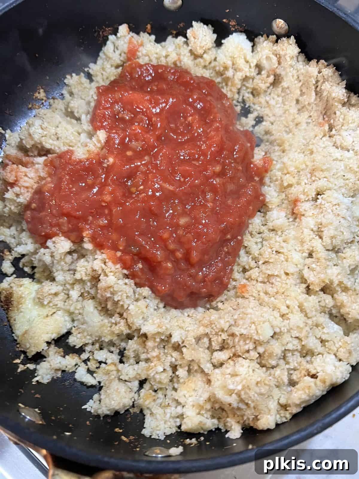 Quick and Flavorful Spanish Cauliflower Rice Bowl with Salsa 11 addition of salsa to cauliflower rice in black pan