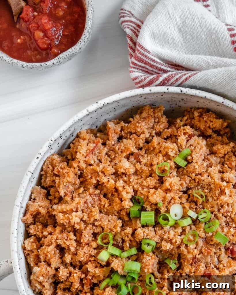 Quick and Flavorful Spanish Cauliflower Rice Bowl with Salsa 13 completed Spanish Cauliflower Rice in a white bowl against a white surface with salsa in the background