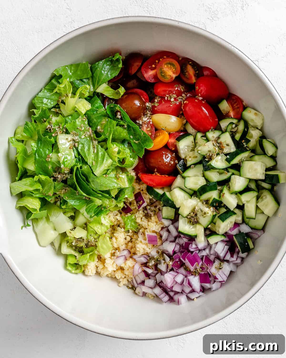 Vibrant Vegan Greek Millet Bowl 13 The exciting process of adding all the freshly prepared ingredients for Vegan Greek Millet Salad into a large white mixing bowl, against a pristine white background.