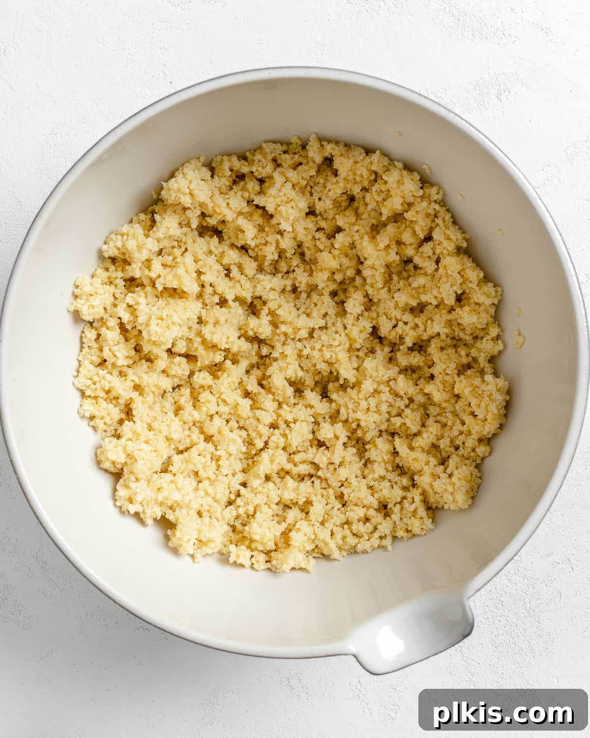 Vibrant Vegan Greek Millet Bowl 7 A bowl of freshly cooked millet, perfectly golden and fluffy, resting in a white bowl against a minimalist white background.