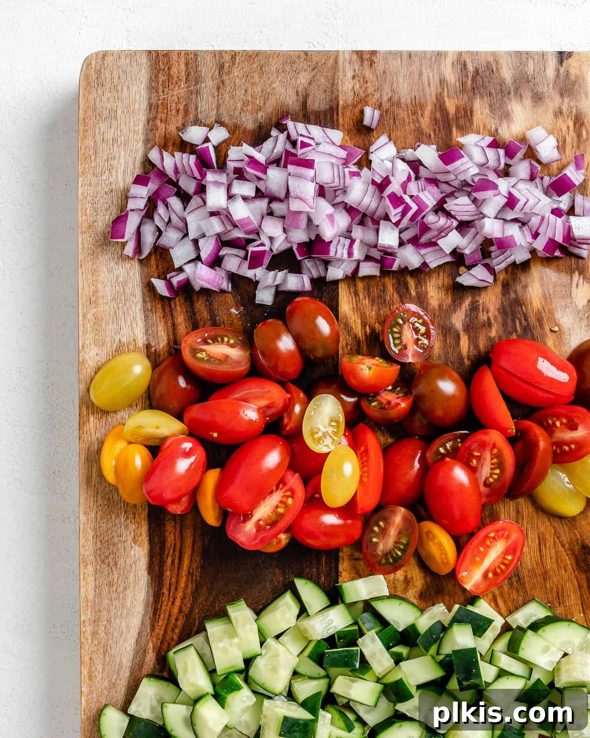 Vibrant Vegan Greek Millet Bowl 9 Neatly chopped red onion, sliced cherry tomatoes, and perfectly cubed cucumber arranged on a rustic wood cutting board, ready for the salad.