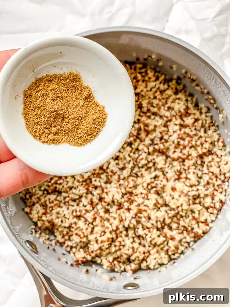 Hearty Quinoa Black Bean Burritos 4 process shot showing adding seasoning to pot during quinoa preparation