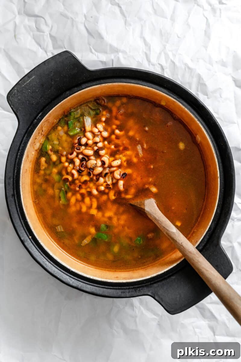 Soulful Vegan Black Eyed Pea Soup 6 Process shot showing the vegan black eyed pea soup simmering in a large pot, with a spoon stirring the rich, hearty mixture.
