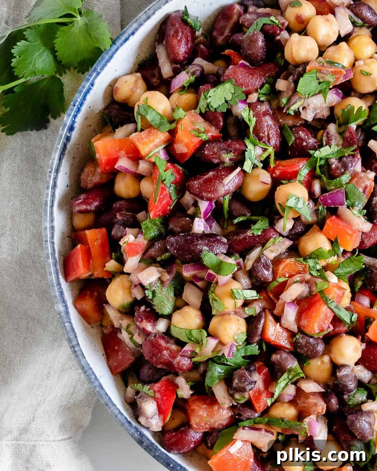 Completed mixed bean salad in a serving bowl with fresh ingredients scattered around against a white background.