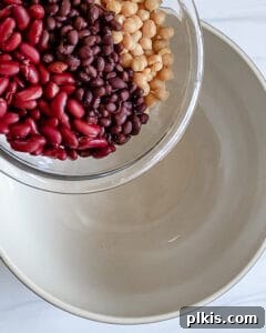 Adding beans and fresh vegetables to a white mixing bowl.