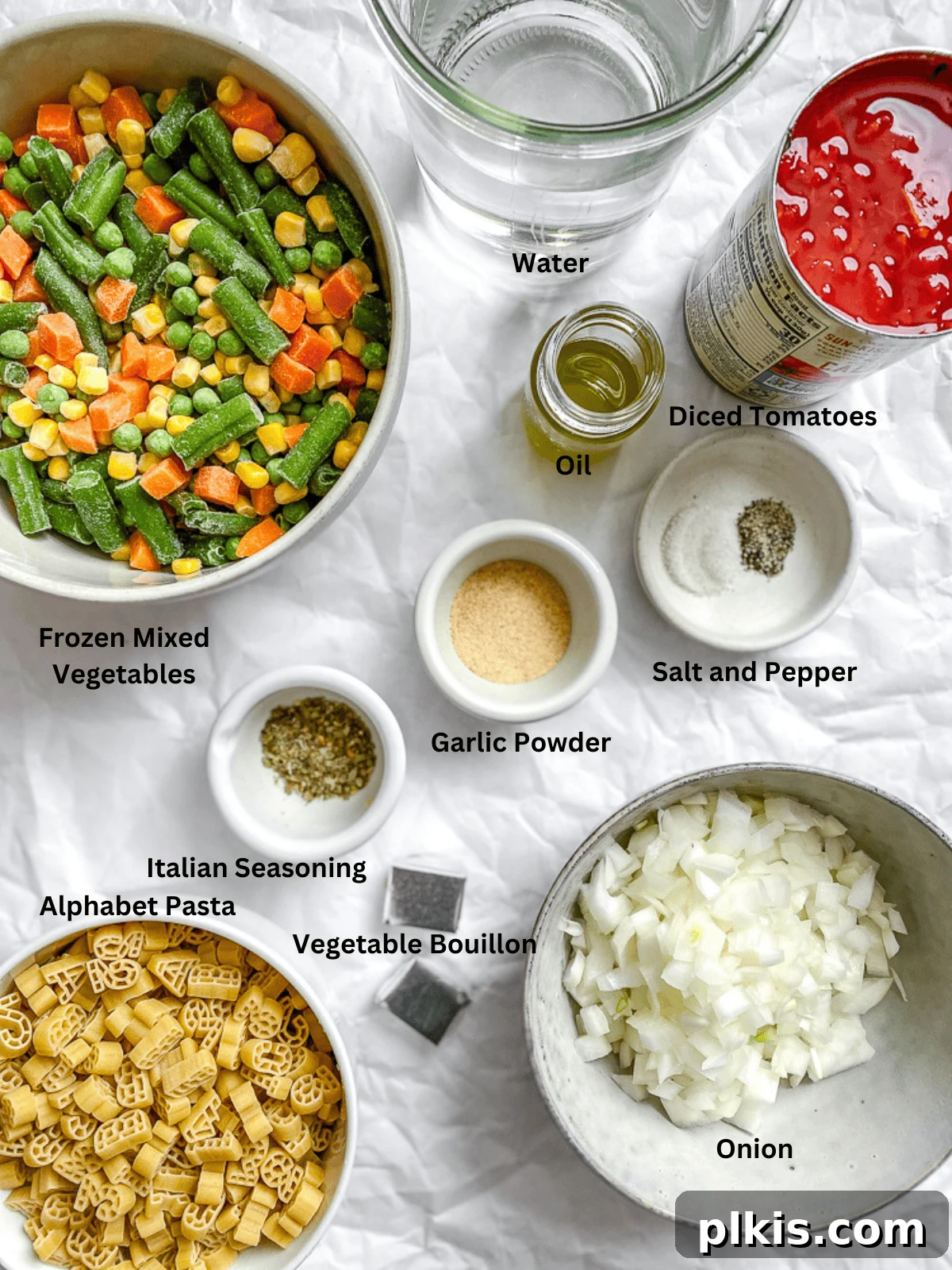 Various alphabet soup ingredients, including diced tomatoes, alphabet pasta, mixed vegetables, and spices, laid out on a white surface.