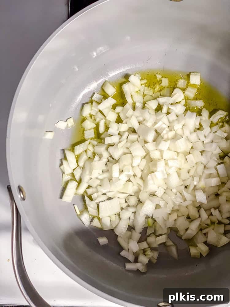 Process shot showing diced onions being sautéed in a large pot with oil until fragrant.