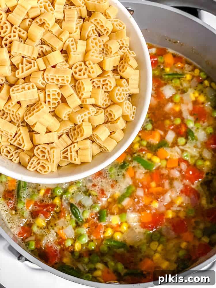 Process shot showing alphabet pasta being stirred into the simmering vegetable and tomato broth.