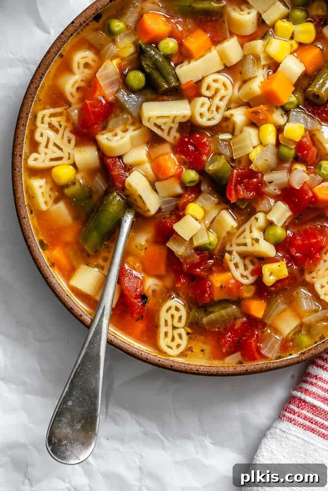 A close-up shot of the finished alphabet soup served in a rustic bowl, garnished with fresh herbs.