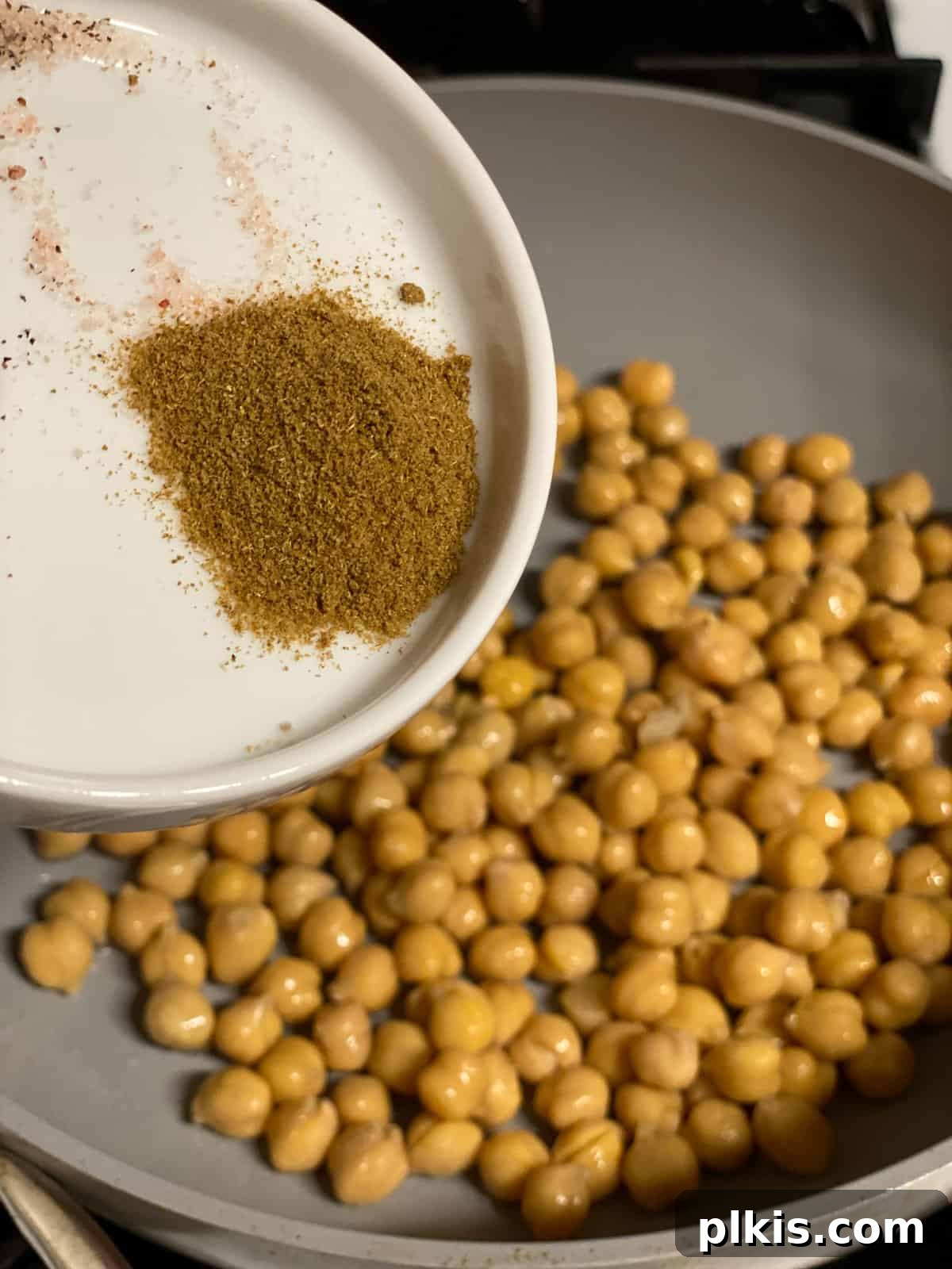 Golden Potato and Chickpea Tacos 9 Process shot of cumin being sprinkled over chickpeas in a frying pan.