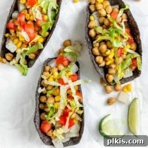 A beautiful close-up of three completed Potato and Chickpea Tacos, garnished with fresh toppings, on a white surface, ready to be enjoyed.