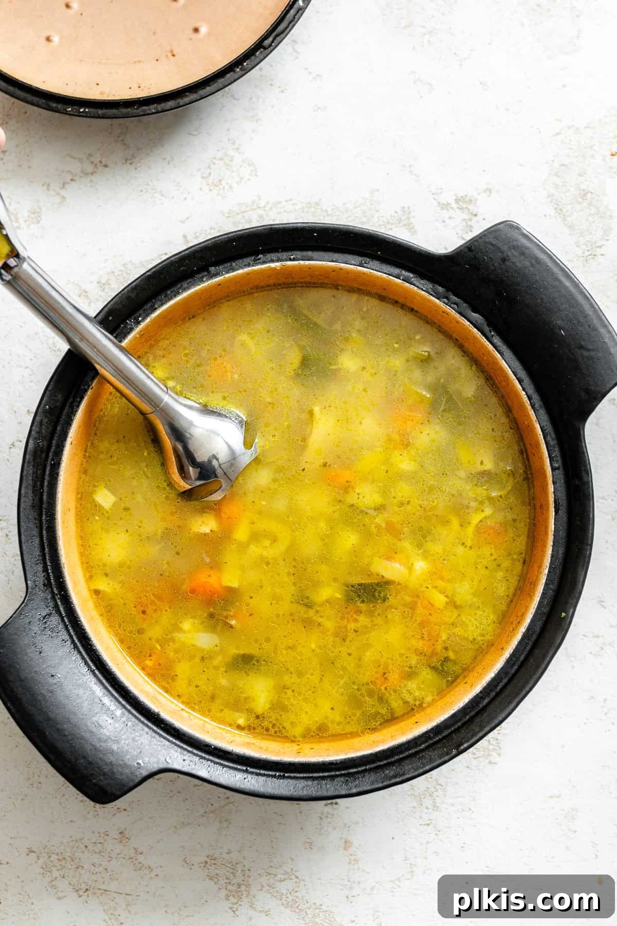 Hearty Vegan Potato and Vegetable Soup 6 An immersion blender being used to puree part of the potato and vegetable soup directly in the pot, creating a creamy texture while leaving some chunks.