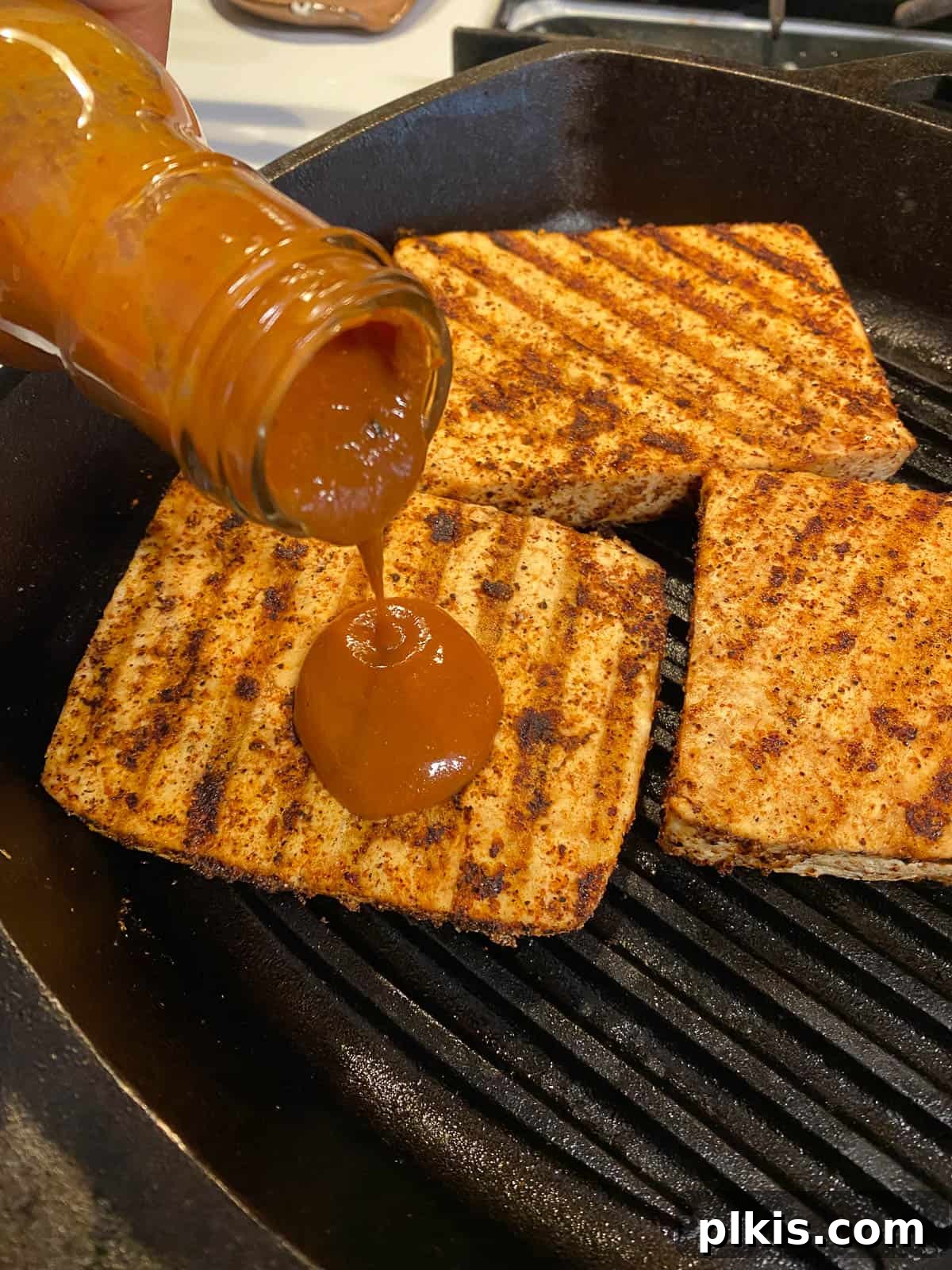 Next-Level Grilled Tofu Steaks 11 Close-up of barbecue sauce being brushed onto grilled tofu slices on the grill, creating a delicious glaze