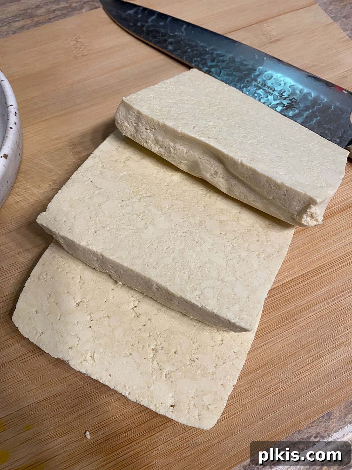 Next-Level Grilled Tofu Steaks 5 Three thick slices of pressed tofu neatly arranged on a cutting board, ready for seasoning