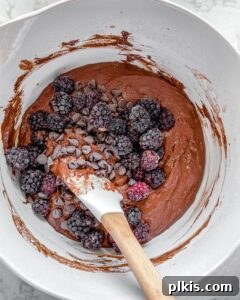Blackberries and dairy-free chocolate chips being folded into the Vegan Blackberry Chocolate Cupcakes batter in a white bowl.