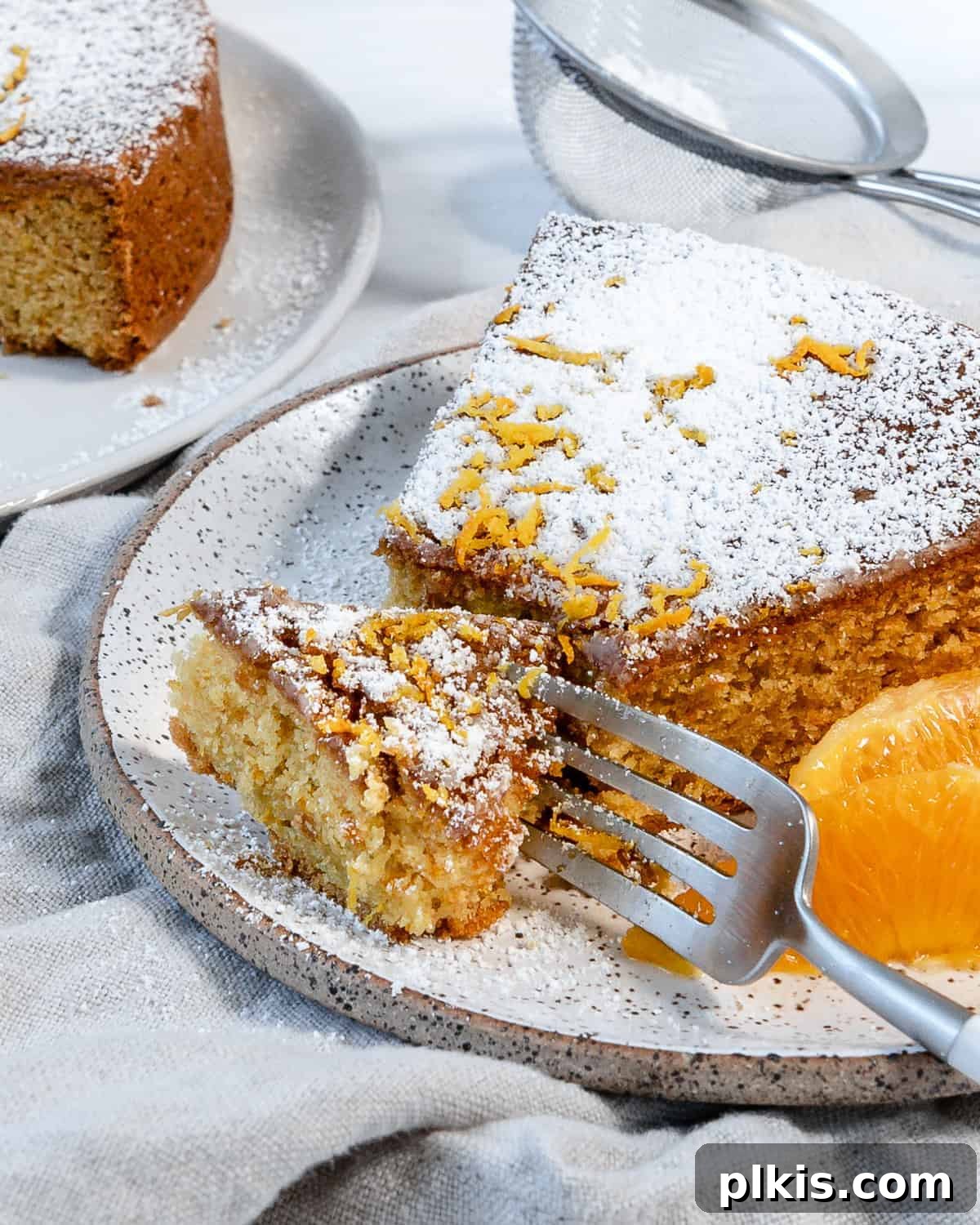 Sun-Kissed Orange Olive Oil Cake 2 A beautifully sliced Orange Olive Oil Cake, showcasing its moist texture and citrus zest, against a pristine white background. Each detail highlights its rich, buttery feel, a testament to its vegan preparation.