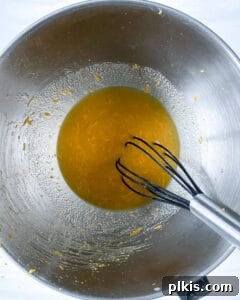 Sun-Kissed Orange Olive Oil Cake 5 Wet ingredients for Orange Olive Oil Cake being mixed in a stainless steel bowl, creating a smooth, vibrant mixture.