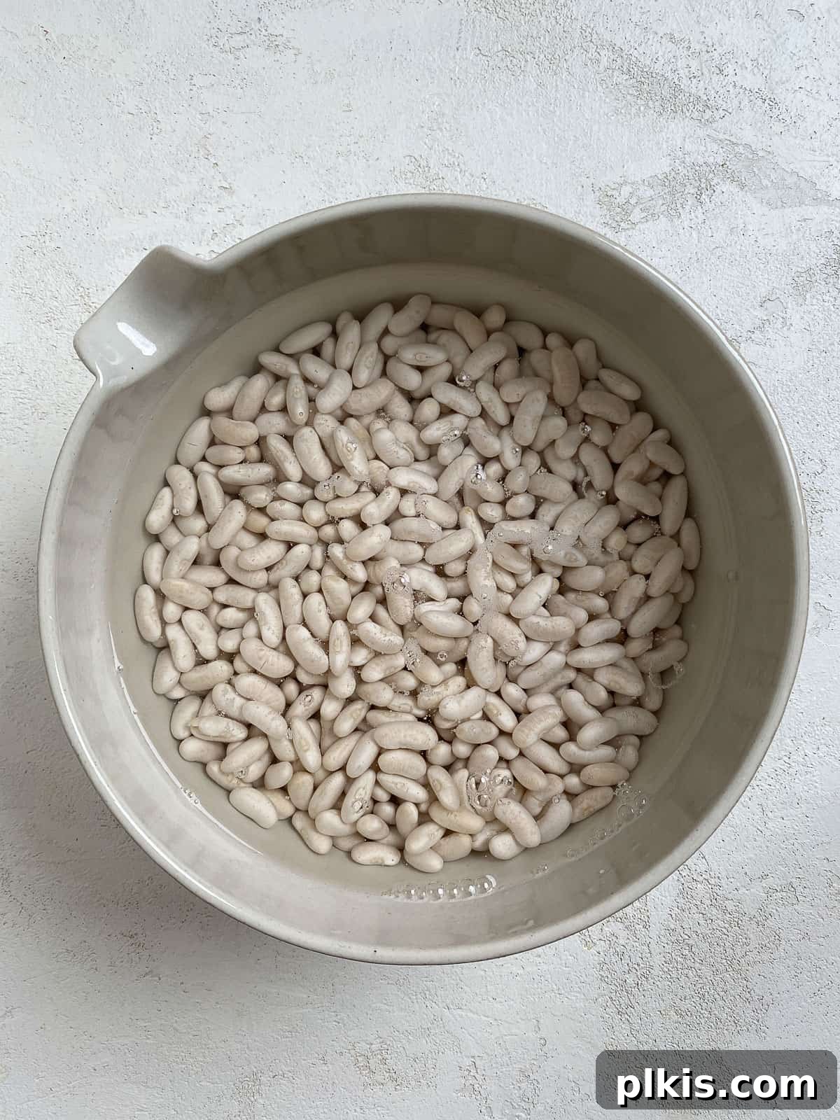 Homestyle Vegan Slow Cooker Baked Beans 5 Process shot of soaked beans in a bowl after draining, ready for cooking, on a white surface