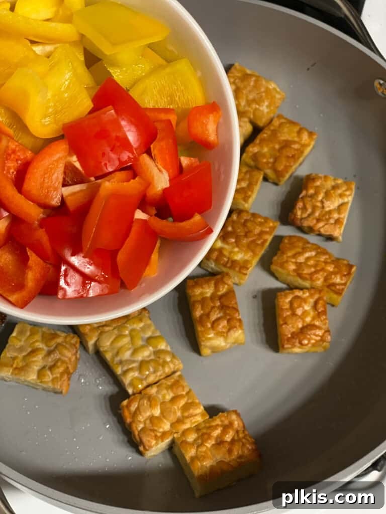 Another process shot of adding bell pepper to the pan, showing a mix of red and yellow.