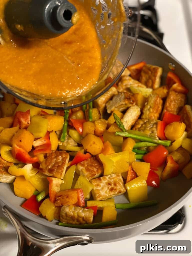 Process shot of pouring the blended pineapple sweet and sour sauce mixture into the pan with tempeh and vegetables.