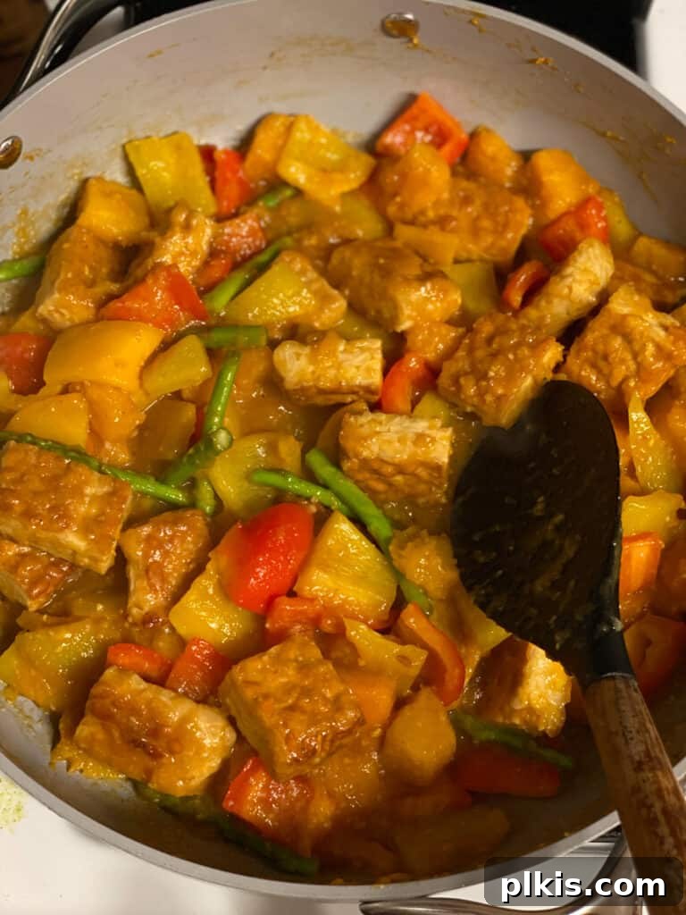 Process shot of mixing the tempeh, vegetables, and sweet and sour sauce together in the pot until thoroughly combined.