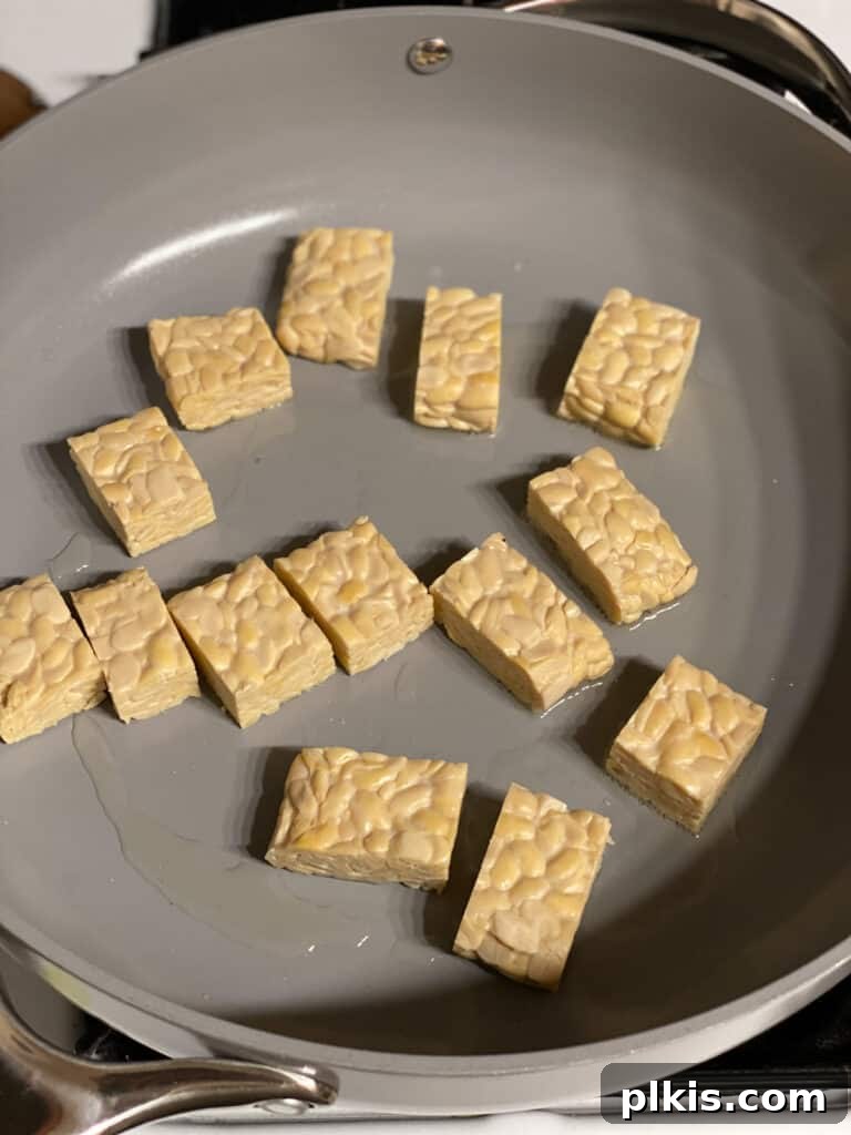 Process shot of tempeh cubes browning in a hot pan, showing a crispy texture.