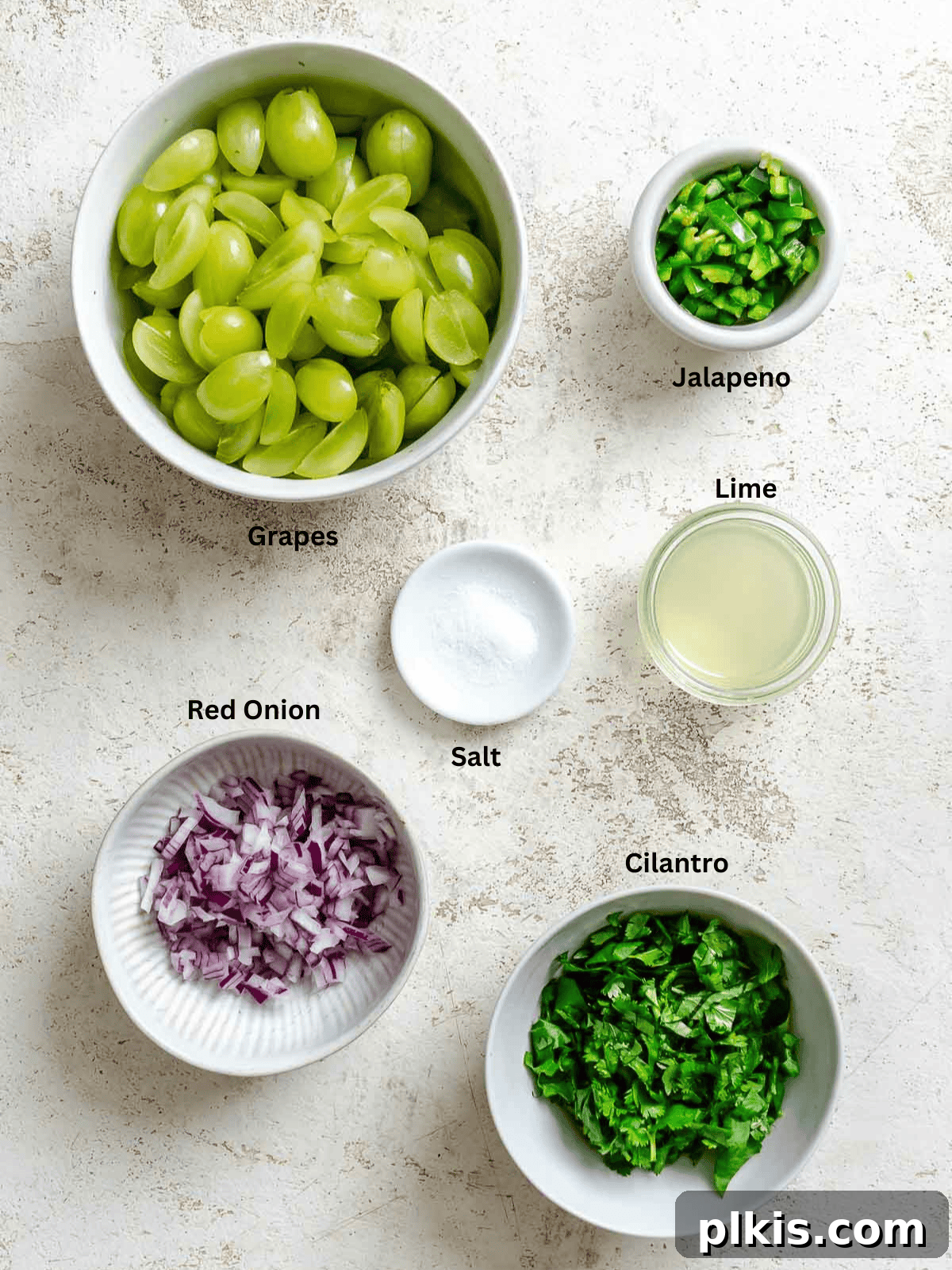 Fresh ingredients for Grape Salsa, including green grapes, red onion, jalapeño, cilantro, and lime, laid out on a white surface.