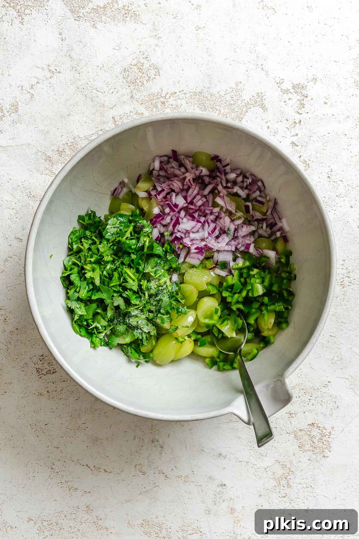 A bowl with chopped green grapes, red onion, and jalapeño, ready for mixing, illustrating the first step of making grape salsa.