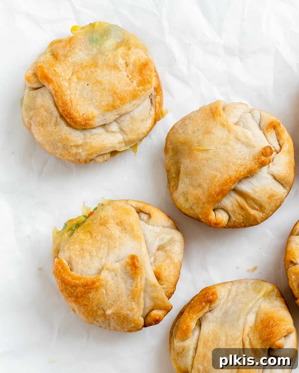 Collection of golden-brown Mini Vegan Pot Pies scattered on a clean white surface, showcasing their bite-sized appeal.