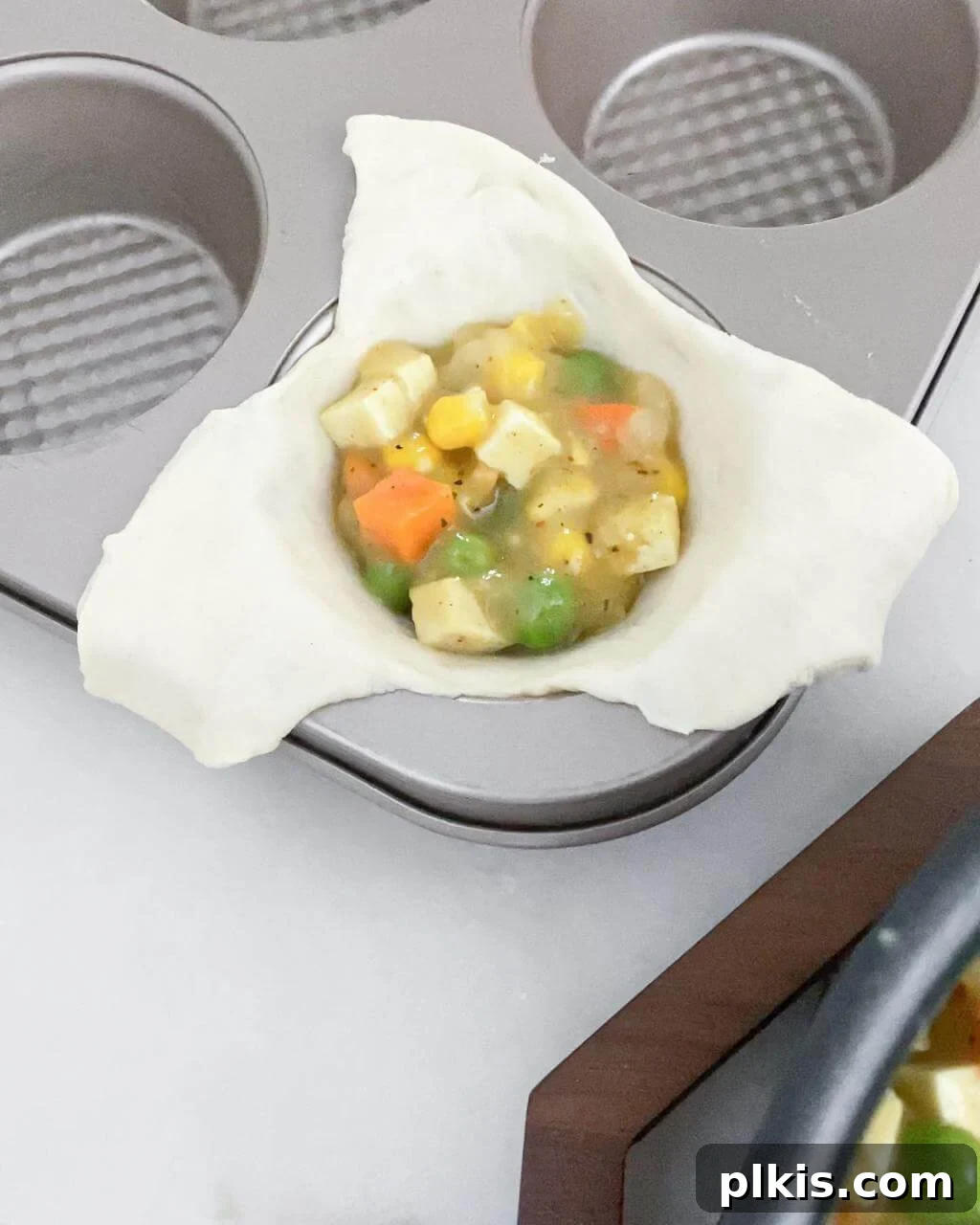 A muffin tin with several mini pot pies assembled, showing the filling nestled in the dough triangles with the corners folded over, ready for baking.