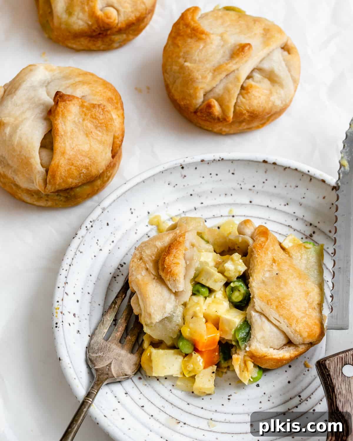 A single Mini Vegan Pot Pie artfully plated with other pies blurred in the background, highlighting its golden crust and delicious presentation.