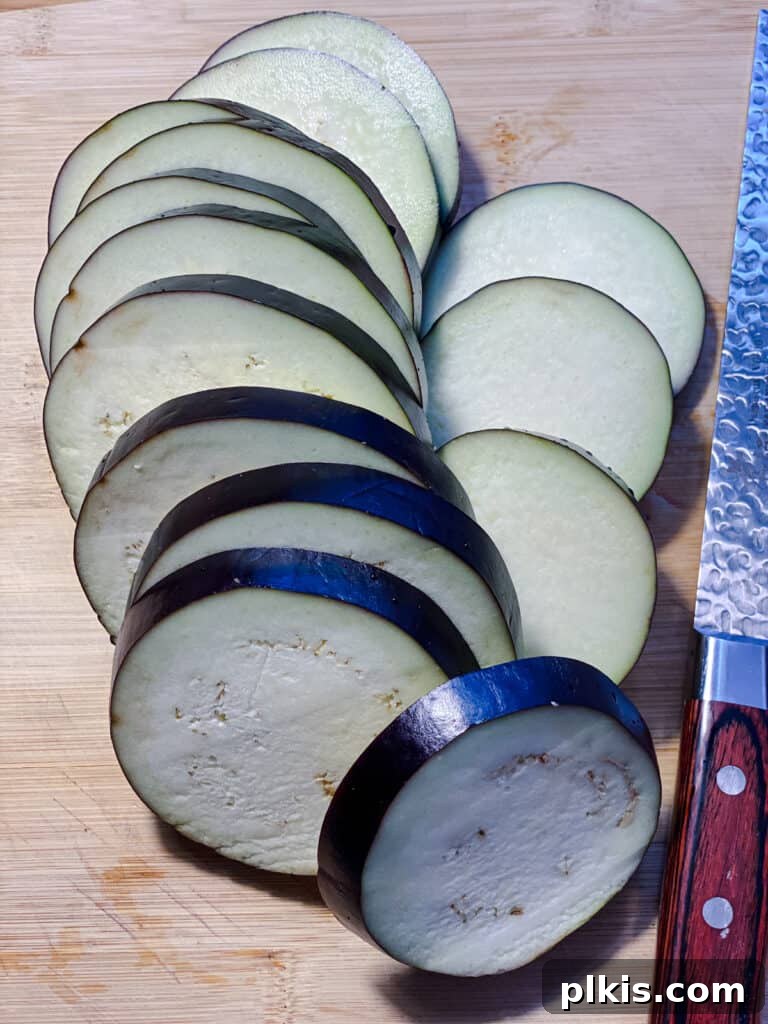 Two Tantalizing Eggplant Stacks 4 Freshly sliced eggplant rounds arranged neatly on a wooden cutting board, ready for seasoning.