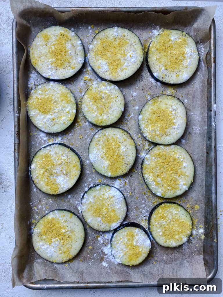 Two Tantalizing Eggplant Stacks 7 Close-up of seasoned eggplant slices on a baking tray, showing the even coating of spices and starch before baking.