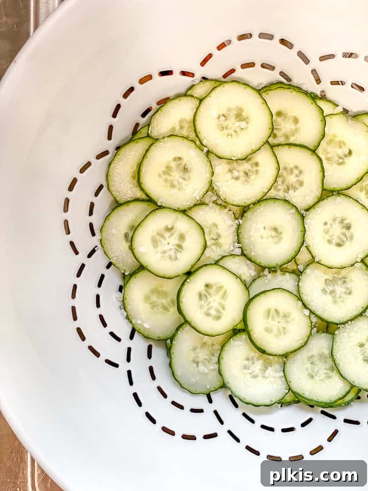 Crisp Cucumber Dill Delight 5 Sliced cucumbers in a white colander, generously sprinkled with salt to draw out excess moisture.