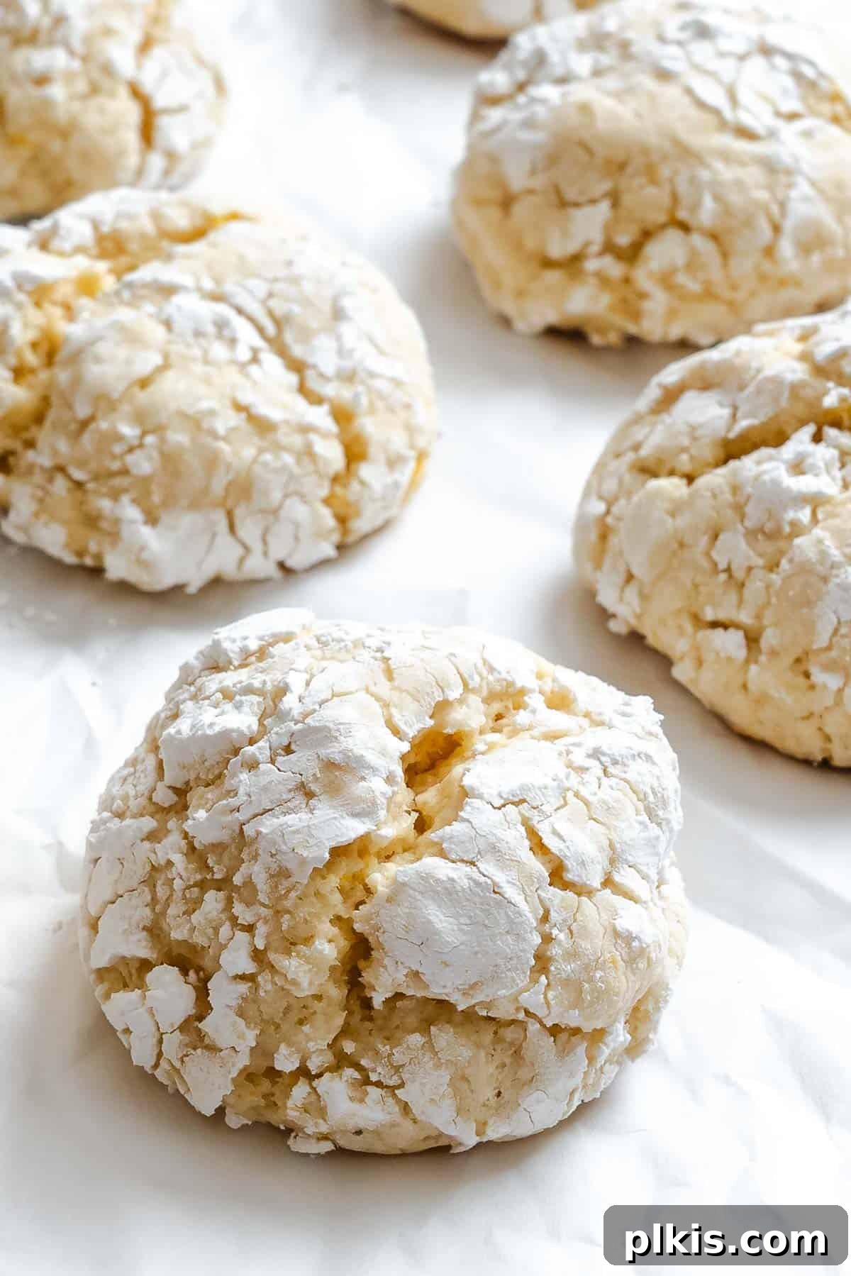 Tangy Lemon Crinkle Delights 2 Beautifully crinkled lemon cookies dusted with powdered sugar, arranged on a white surface.