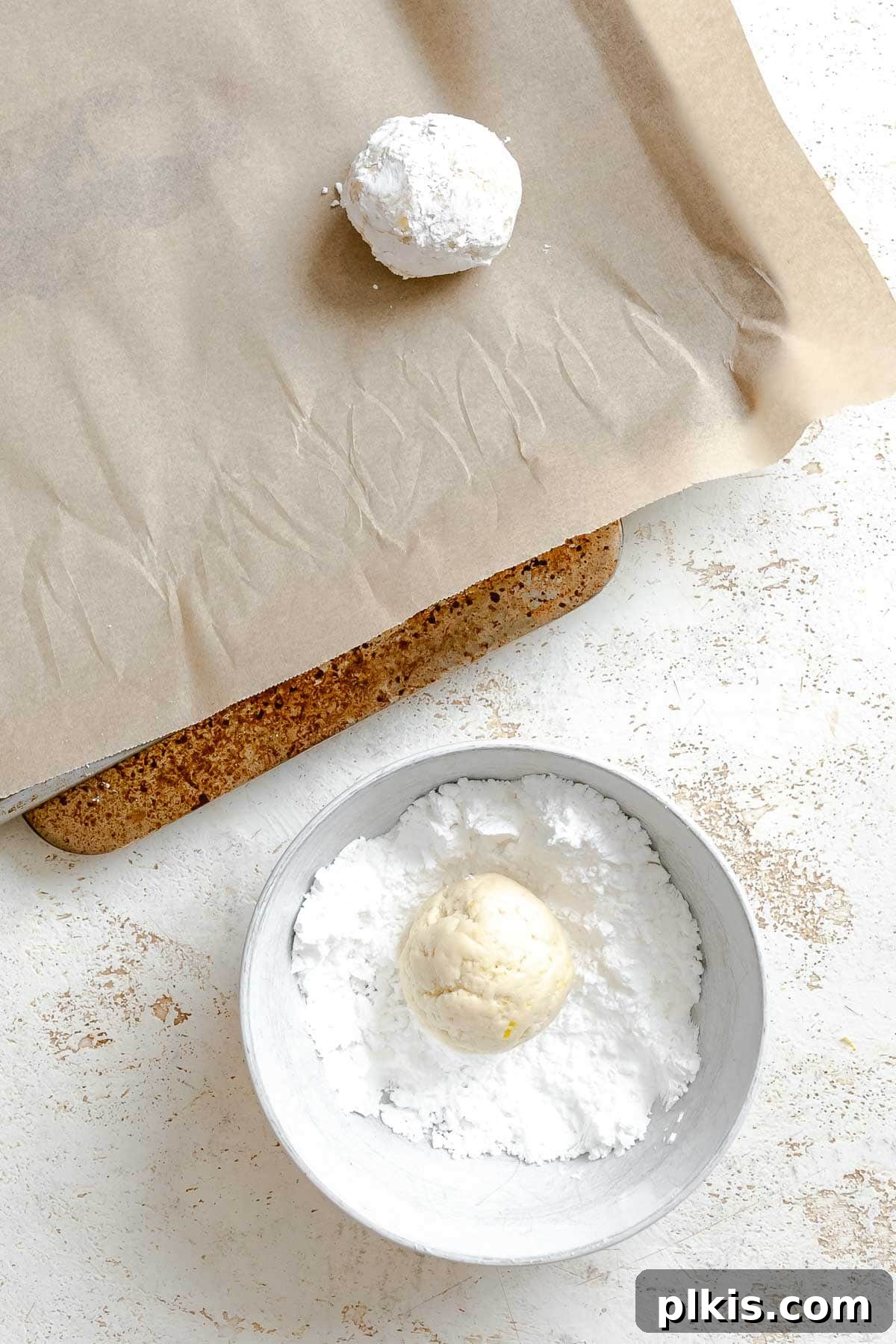 Tangy Lemon Crinkle Delights 7 A ball of cookie dough being generously coated in powdered sugar, highlighting the crinkle cookie preparation.