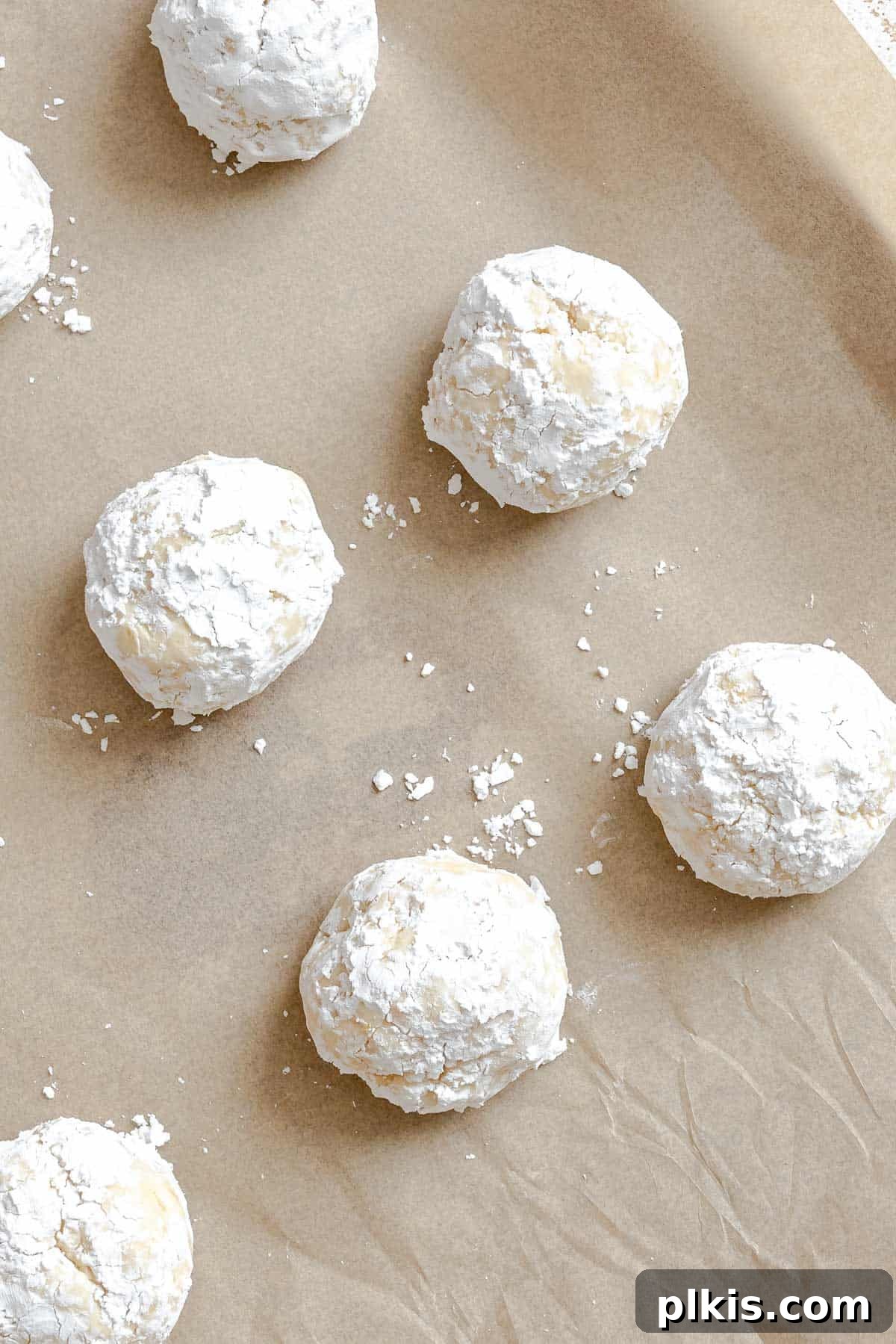 Tangy Lemon Crinkle Delights 8 Neatly arranged balls of lemon crinkle cookie dough, generously coated in powdered sugar, on a baking sheet.
