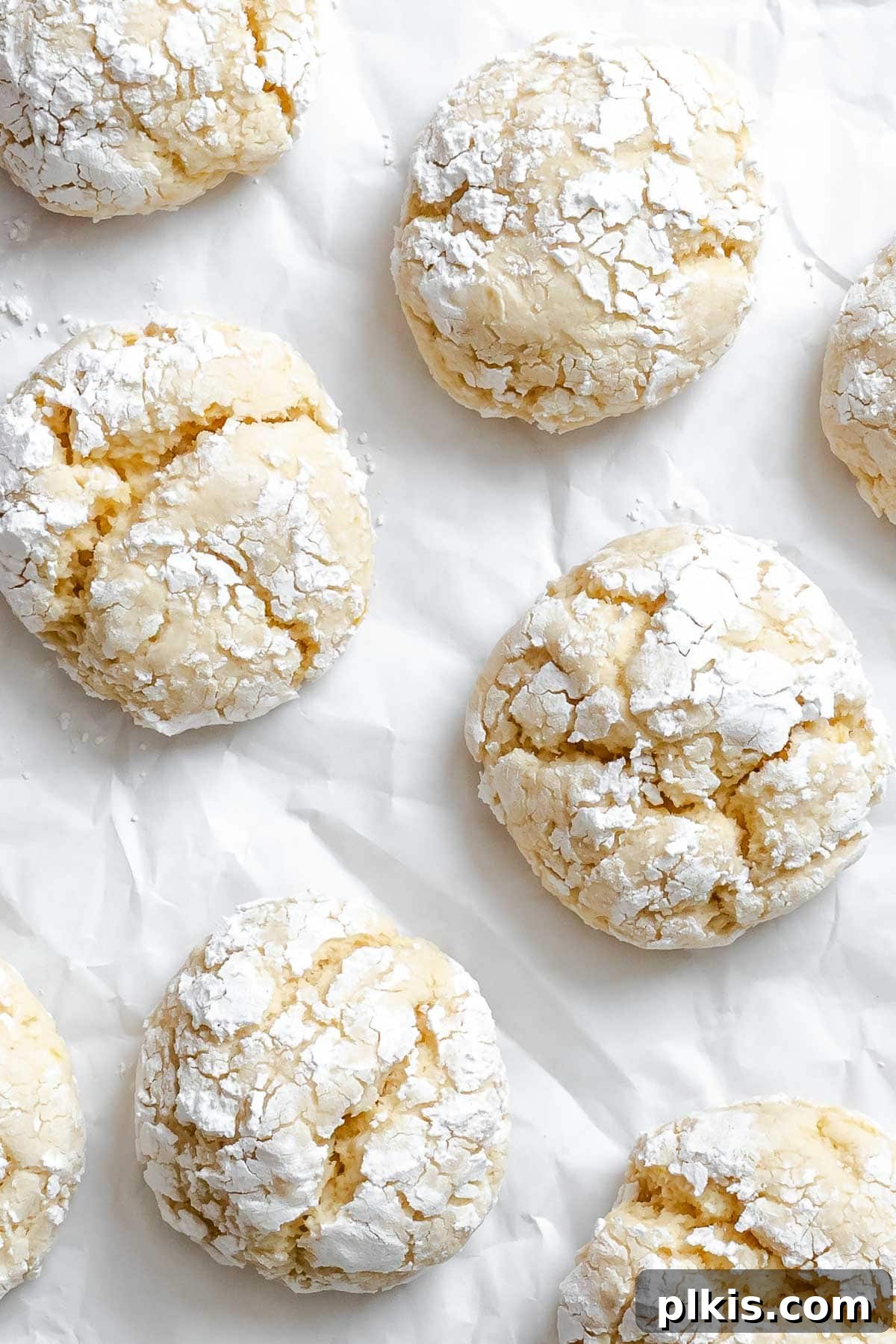 Tangy Lemon Crinkle Delights 9 A close-up of perfectly baked lemon crinkle cookies, beautifully cracked and dusted with powdered sugar, on a white surface.
