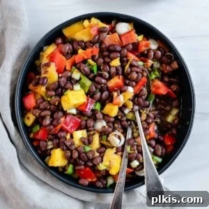 A serving of the delicious mango black bean salad in a dark bowl with a fork, emphasizing its vibrant appearance.