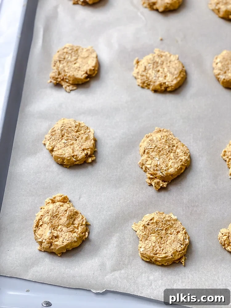 Spiced Pumpkin Oatmeal Cookies 7 Process shot of unbaked pumpkin oatmeal cookie dough balls arranged on a baking sheet lined with parchment paper, gently flattened and spaced apart.