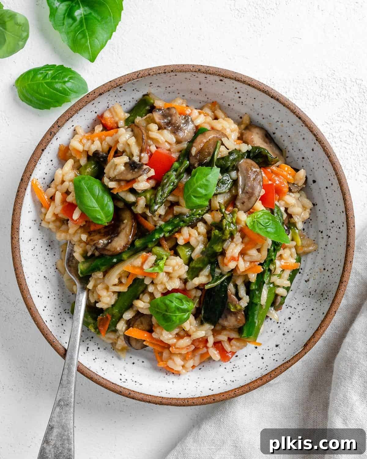 Creamy Vegan Garden Risotto 2 completed vegan risotto plated on a white plate against a white background with spinach in the back