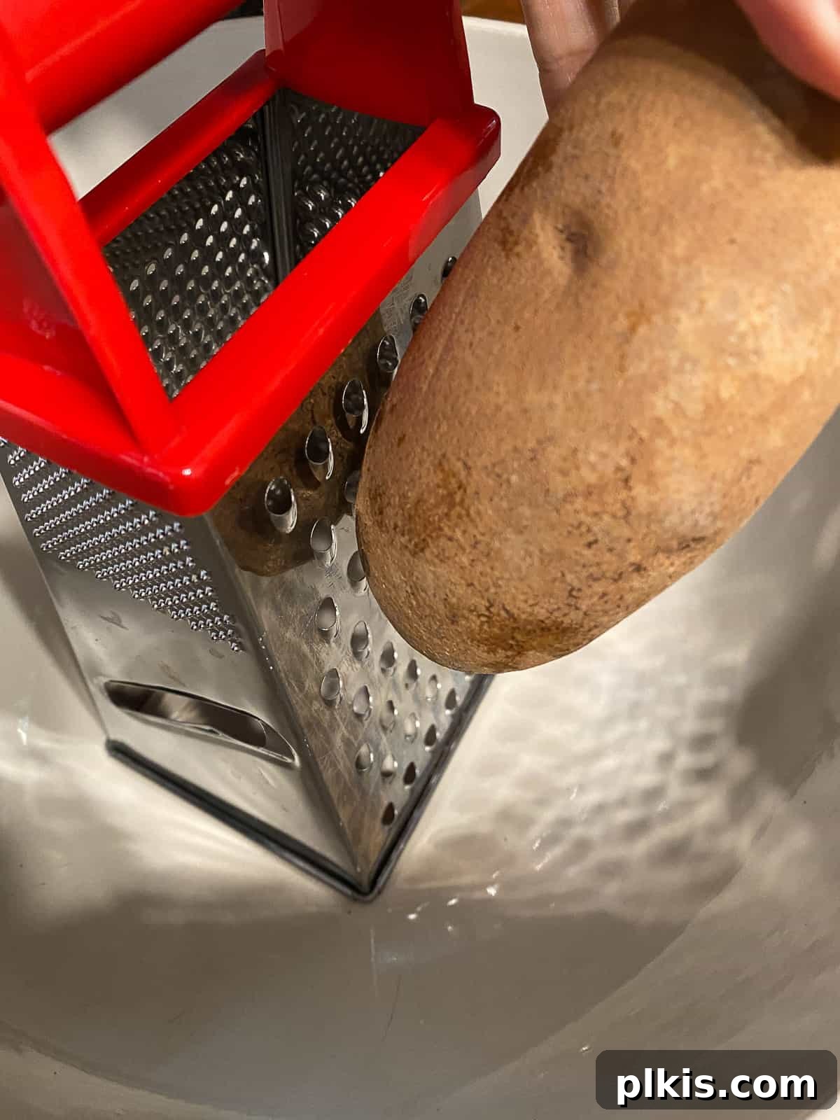Wholesome Red Lentil Burgers 7 Process shot of grating a potato, illustrating the preparation of fresh ingredients.