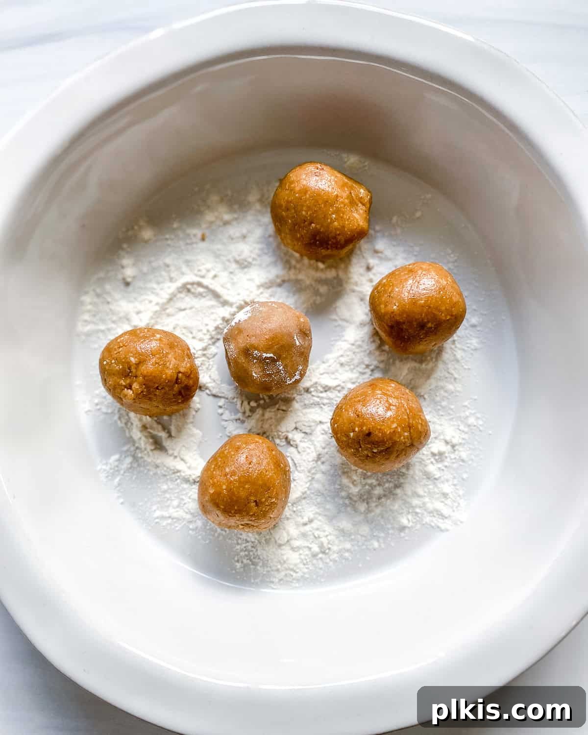 Frightfully Delicious Peanut Butter Spiders 5 Process shot showing rolling small peanut butter balls in flour on a large pan.