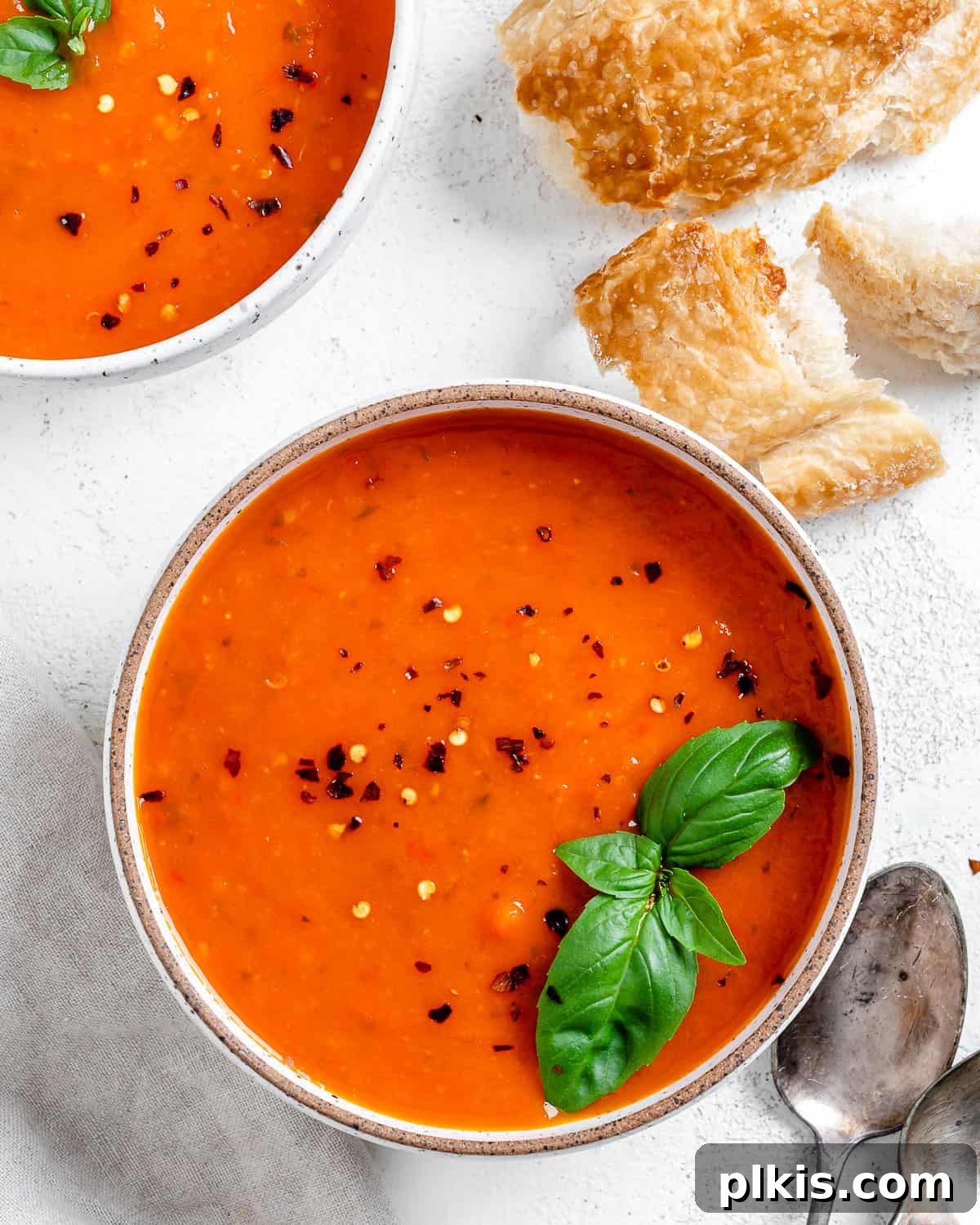 Velvety Vegan Tomato Basil Soup 2 completed Tomato Basil Soup in a bowl against a light surface with ingredients in the background