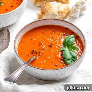 completed Tomato Basil Soup in a bowl against a light surface with ingredients in the background